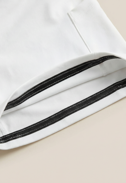 Close-up of a white garment with black trim on a beige background
