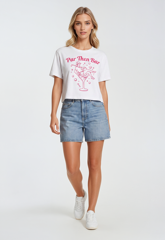 Woman wearing a white Par Then Bar t-shirt with pink text and graphics, paired with denim shorts on a white background