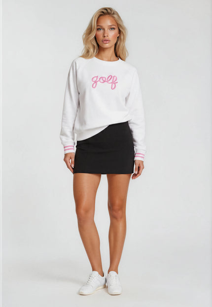 Woman wearing a white sweatshirt with 'golf' printed on it, black skirt, and white sneakers against a white background