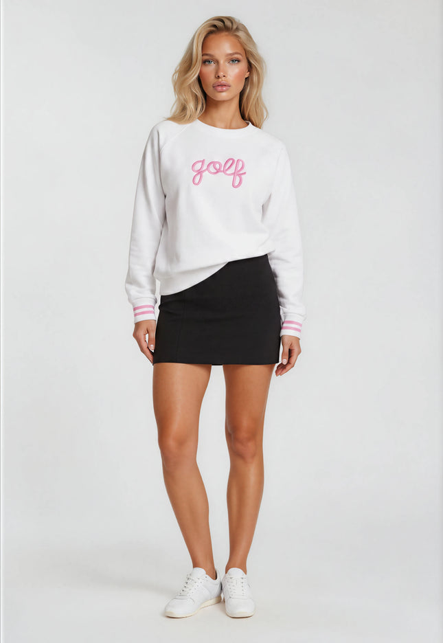 Woman wearing a white sweatshirt with 'golf' printed on it, black skirt, and white sneakers against a white background