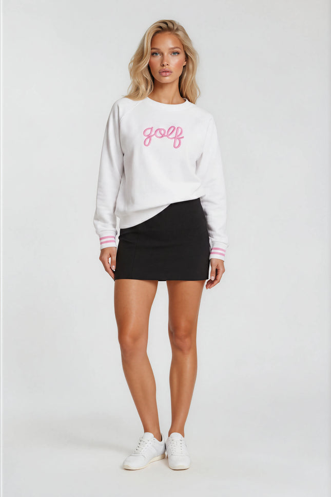 Woman wearing a white sweatshirt with 'golf' printed on it, black skirt, and white sneakers against a white background