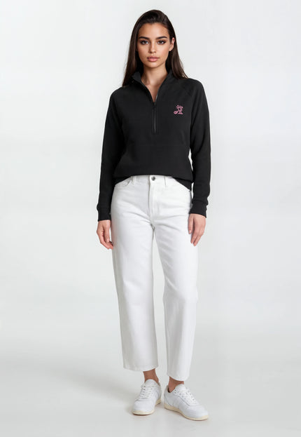 Woman wearing a black sweater with a logo and white pants on a white background