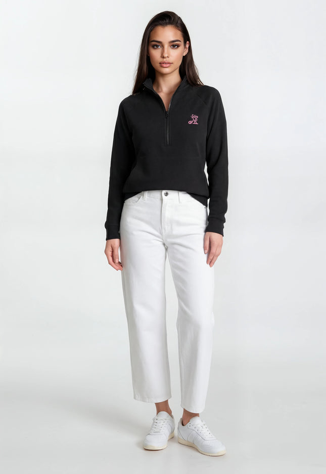 Woman wearing a black sweater with a logo and white pants on a white background