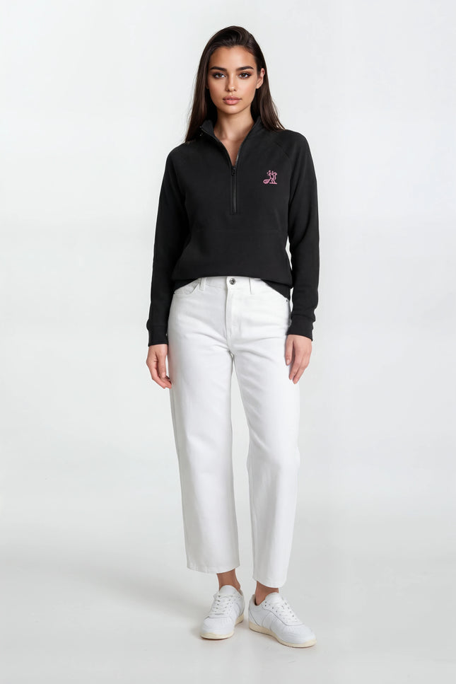 Woman wearing a black sweater with a logo and white pants on a white background